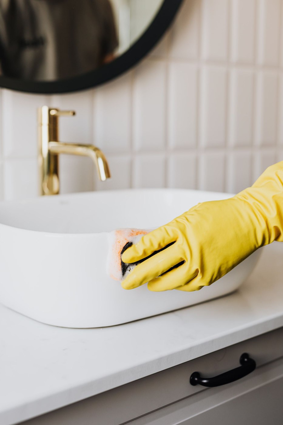 Person in glove wiping surface of sink in bathroom