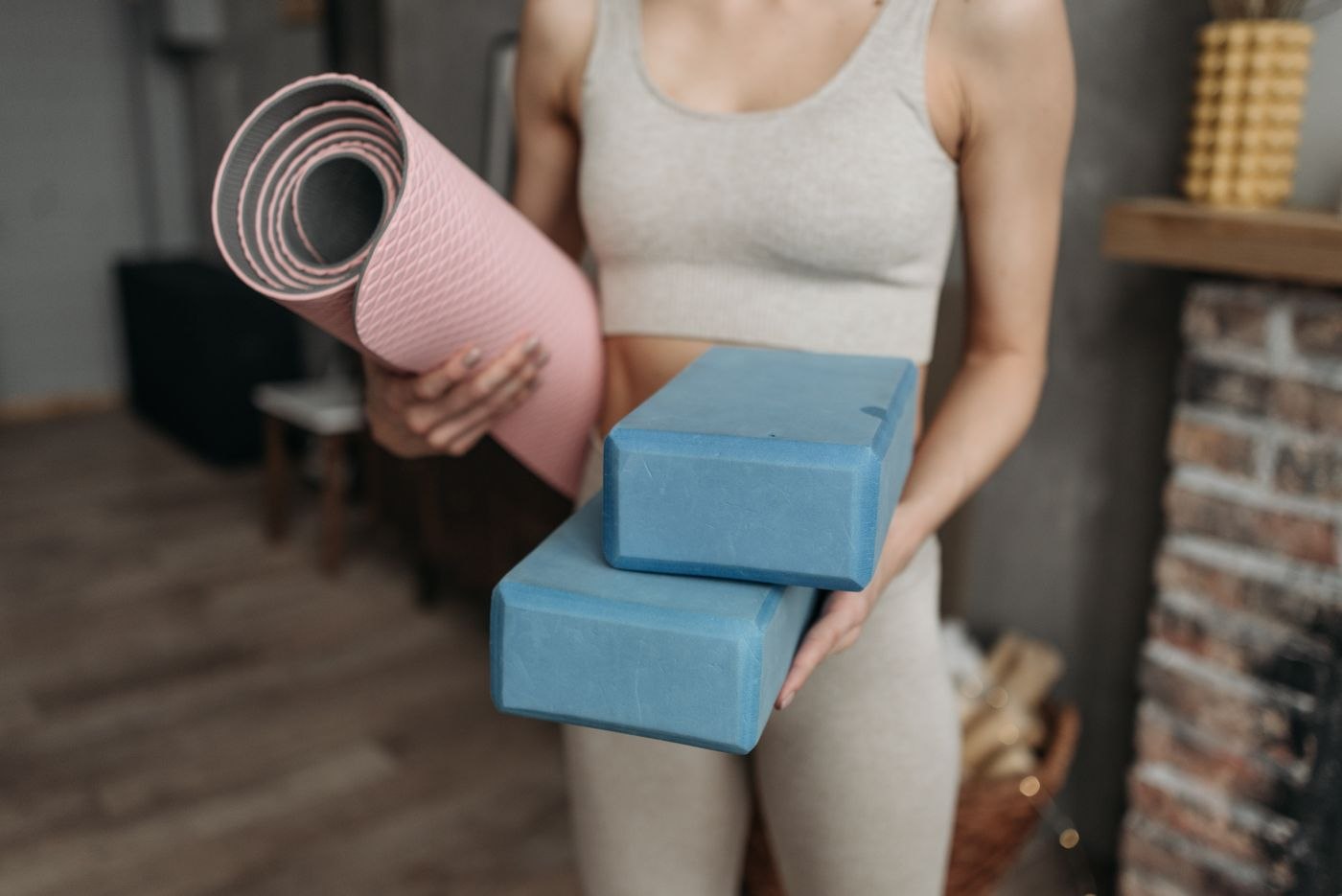 A person holding a rolled exercise mat and foam yoga blocks
